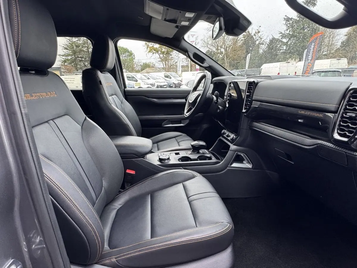 Vue intérieure côté conducteur du Ford Ranger Wildtrak 2025, sièges cuir noirs avec surpiqûres orange et tableau de bord moderne.
