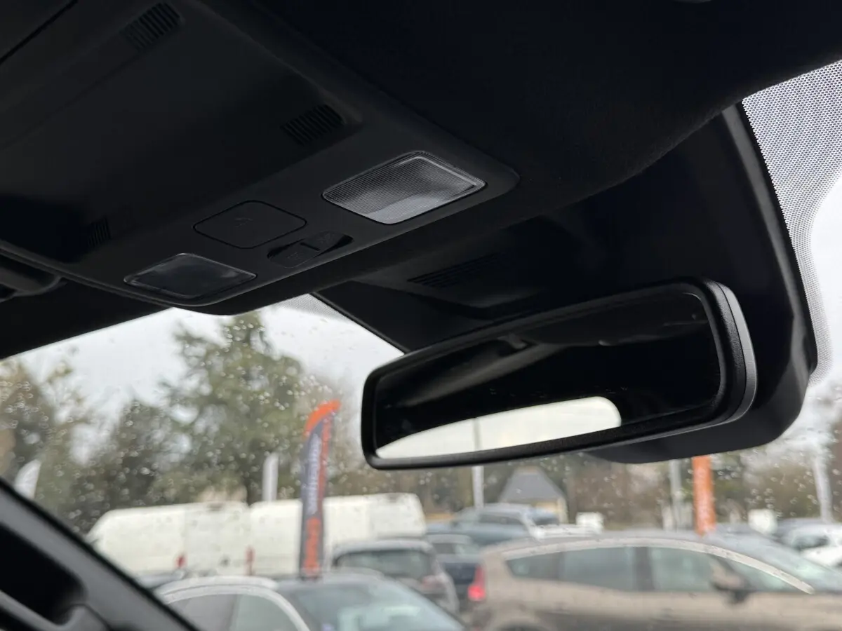 Vue intérieure centrée sur le rétroviseur intérieur et plafonnier noir du Ford Ranger 2025, arrière flou extérieur.