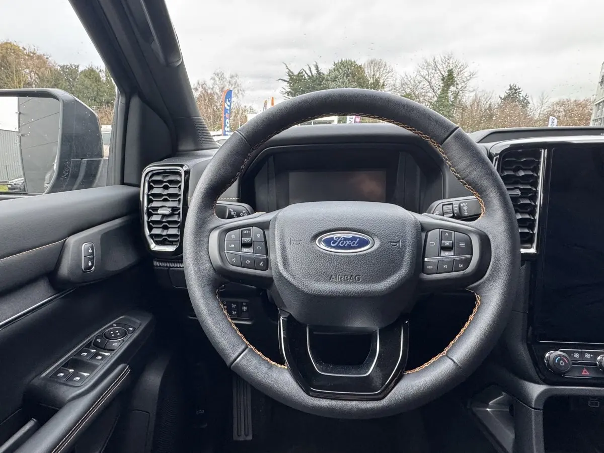 Vue intérieure centrée sur le volant noir en cuir avec surpiqûres marron du Ford Ranger 2025, tableau de bord visible.