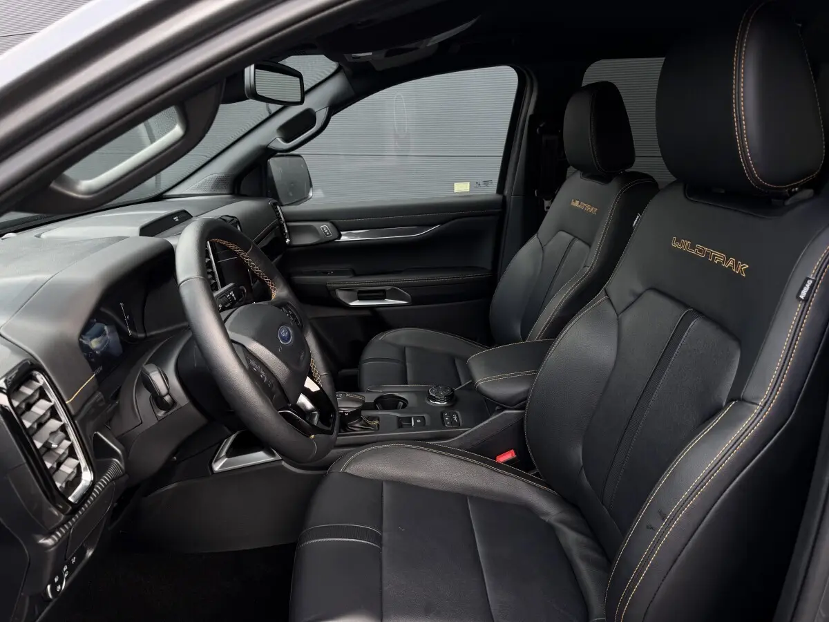 Vue intérieure côté conducteur du Ford Ranger Wildtrak 2025, sièges noirs en cuir avec surpiqûres orange et logo brodé.