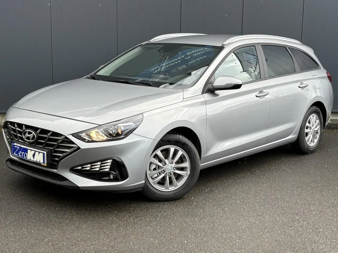 Hyundai i30 SW T-GDI 120 Modern gris argent en 3/4 avant droit, avec jantes alliage et rails de toit visibles.