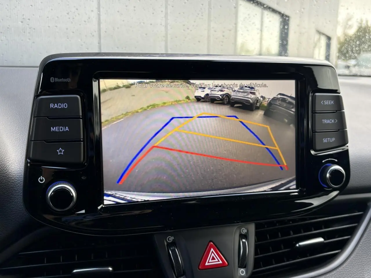Écran tactile de la Hyundai i30 SW T-GDI 120 Modern affichant la caméra de recul avec lignes de guidage colorées.