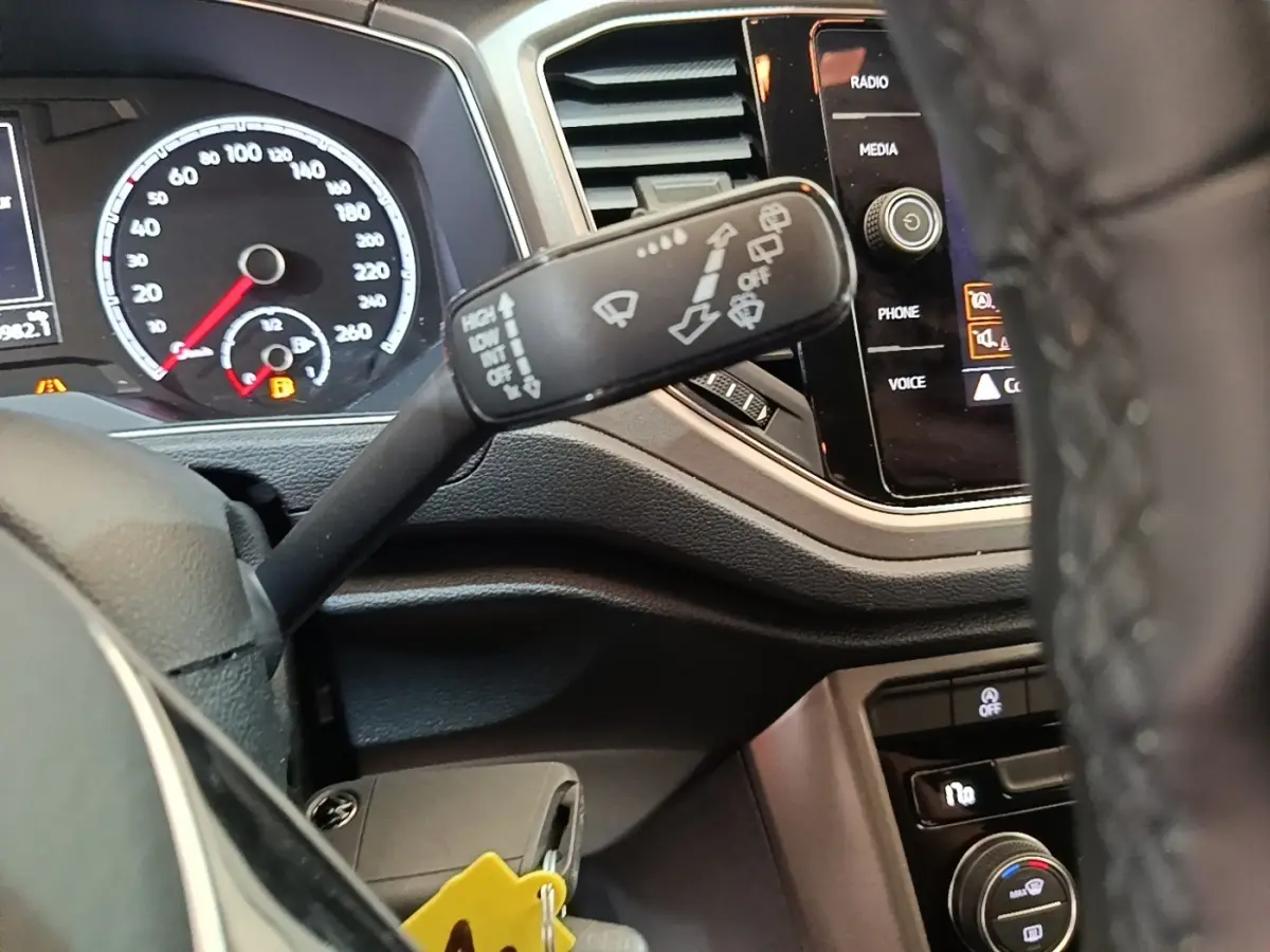 Gros plan sur la manette d’essuie-glace du Volkswagen T-Roc 1.5 TSI, tableau de bord et écran tactile visibles.