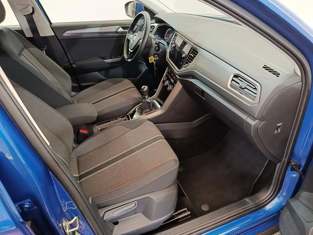 Vue intérieure côté conducteur du Volkswagen T-Roc bleu 2020, montrant sièges tissu et tableau de bord moderne avec écran tactile.