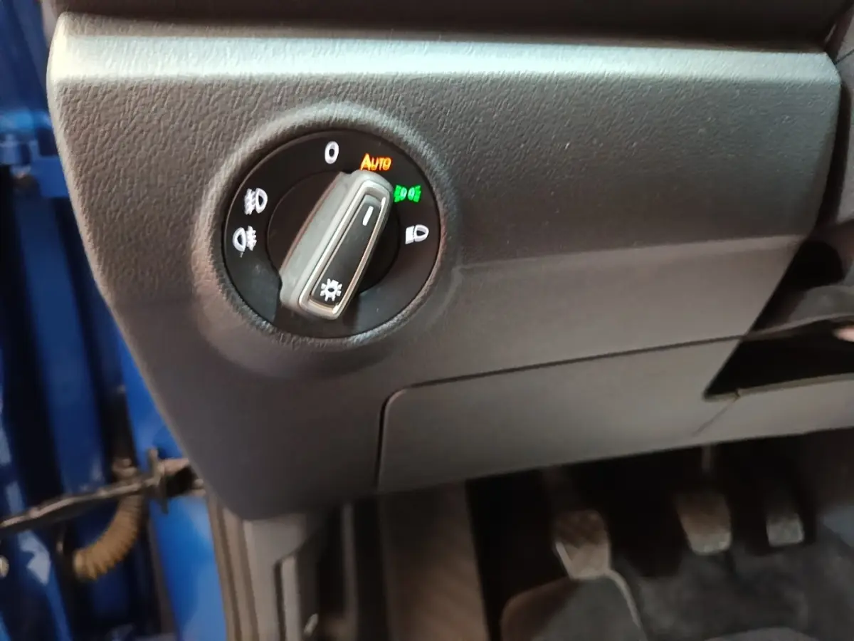 Gros plan sur le bouton de commande des phares à gauche du volant dans un Volkswagen T-Roc bleu 2020, intérieur noir.