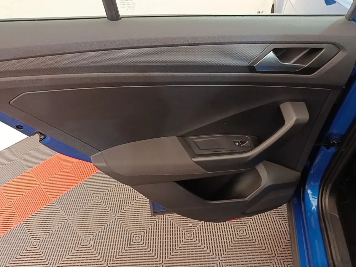 Vue rapprochée de la porte avant gauche bleu vif d’un Volkswagen T-Roc 1.5 TSI avec poignée et bouton de vitre électrique.