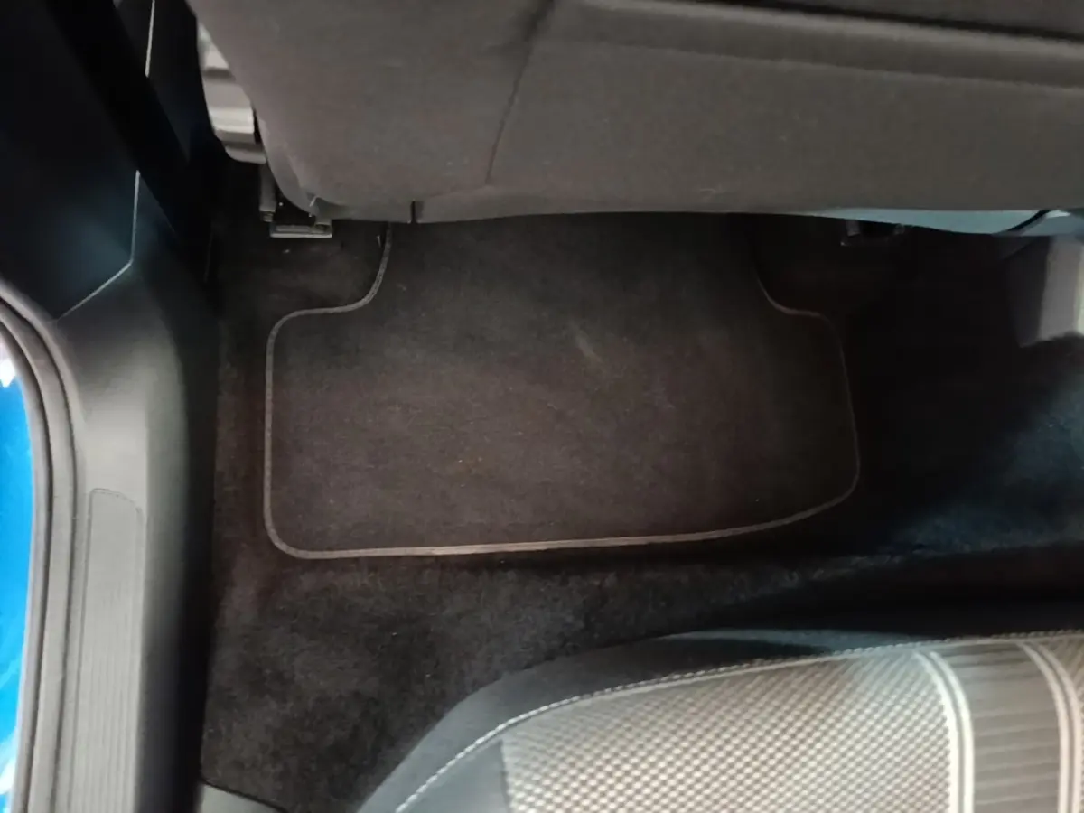 Vue intérieure du plancher arrière côté gauche du Volkswagen T-Roc bleu, avec tapis de sol noir et siège tissu gris.