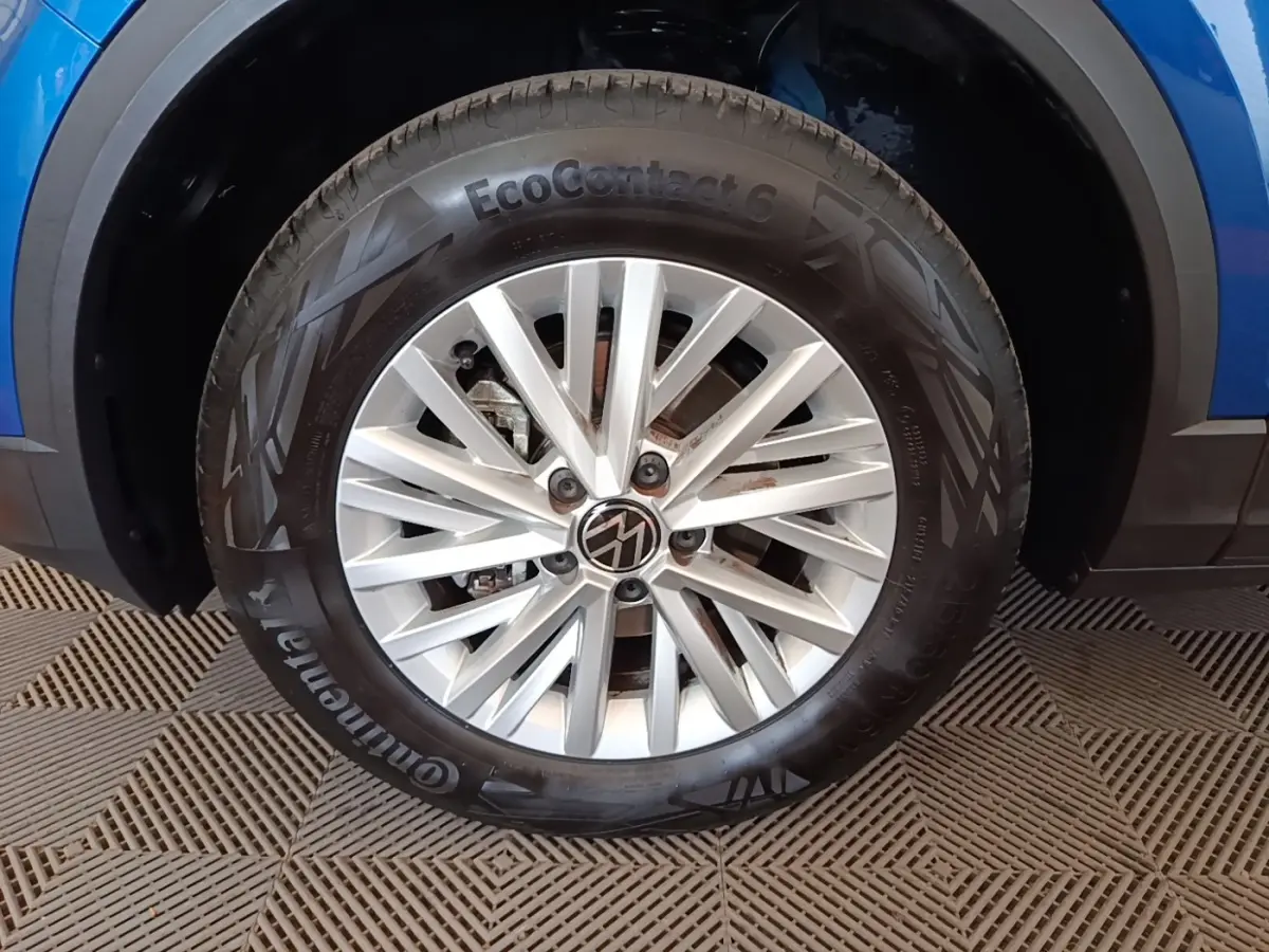 Gros plan sur la roue avant droite d’un Volkswagen T-Roc bleu, jante alliage argentée avec logo VW central.