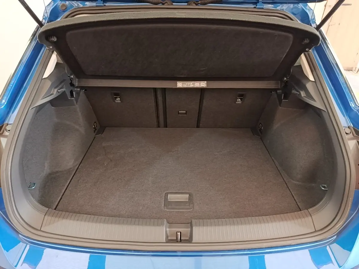 Coffre ouvert vu de l'arrière d'un Volkswagen T-Roc bleu 1.5 TSI 150 EVO UNITED, espace de chargement vide et tapis gris.