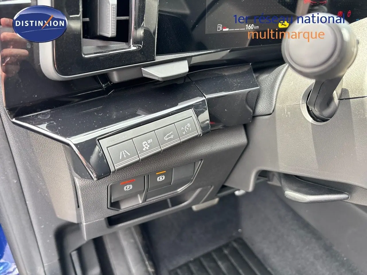 Gros plan sur les commandes sous le tableau de bord du Renault Austral bleu Iron Metal, avec boutons d'assistance et frein à main électrique.