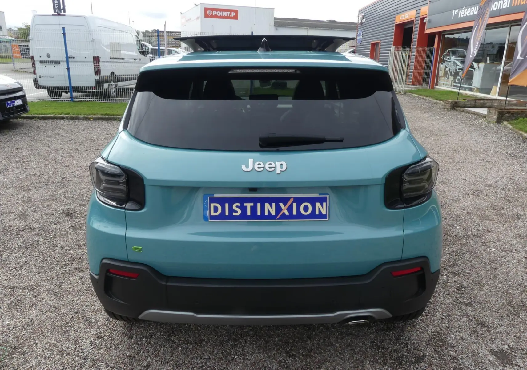 Vue arrière d'un Jeep Avenger bleu métallisé avec feux arrière fumés et plaque Distinxion sur un parking.