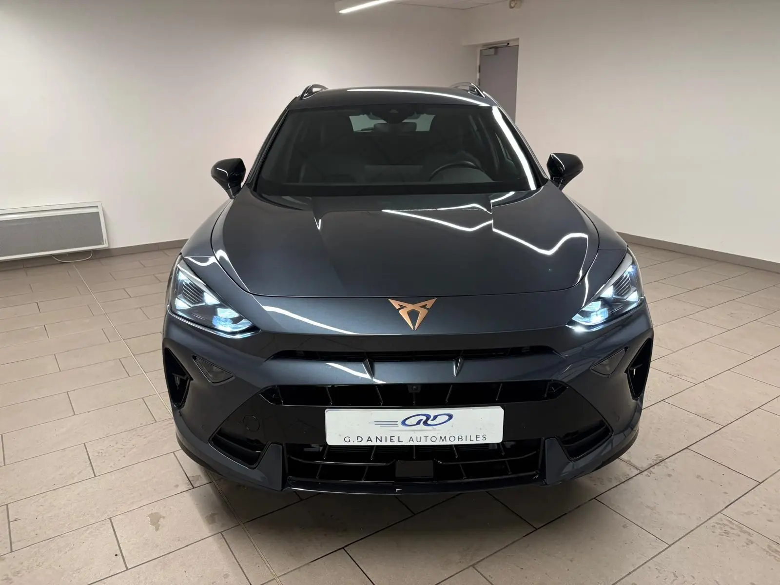 Vue frontale d'un CUPRA Formentor gris magnétique avec phares allumés et logo cuivré sur le capot.