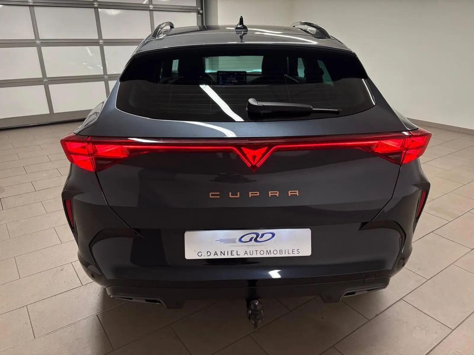 Vue arrière d'un CUPRA Formentor gris magnétique avec feux LED reliés et crochet d'attelage escamotable visible.