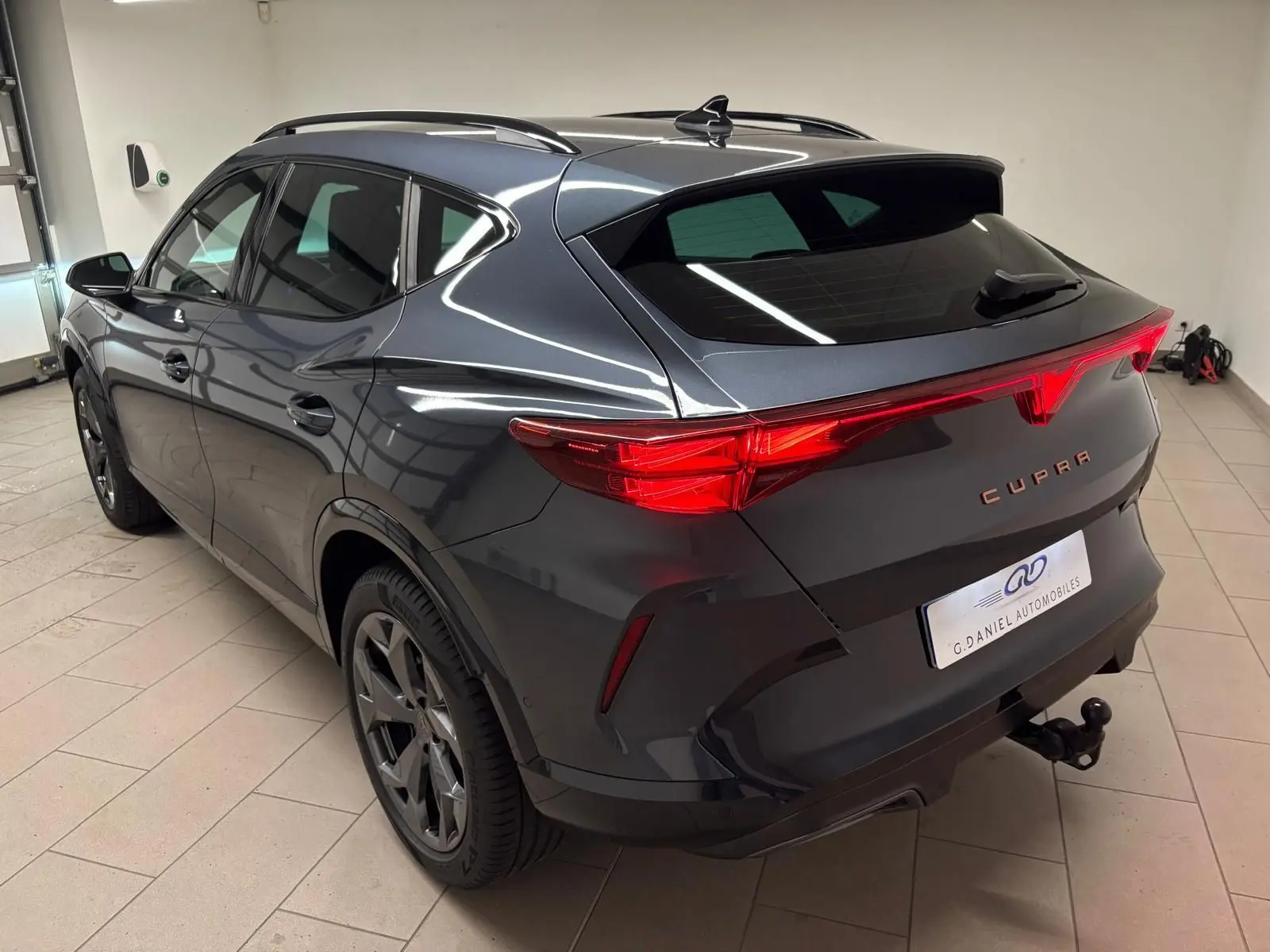 Vue 3/4 arrière droite d'un CUPRA Formentor gris magnétique avec attelage escamotable et feux arrière allumés.