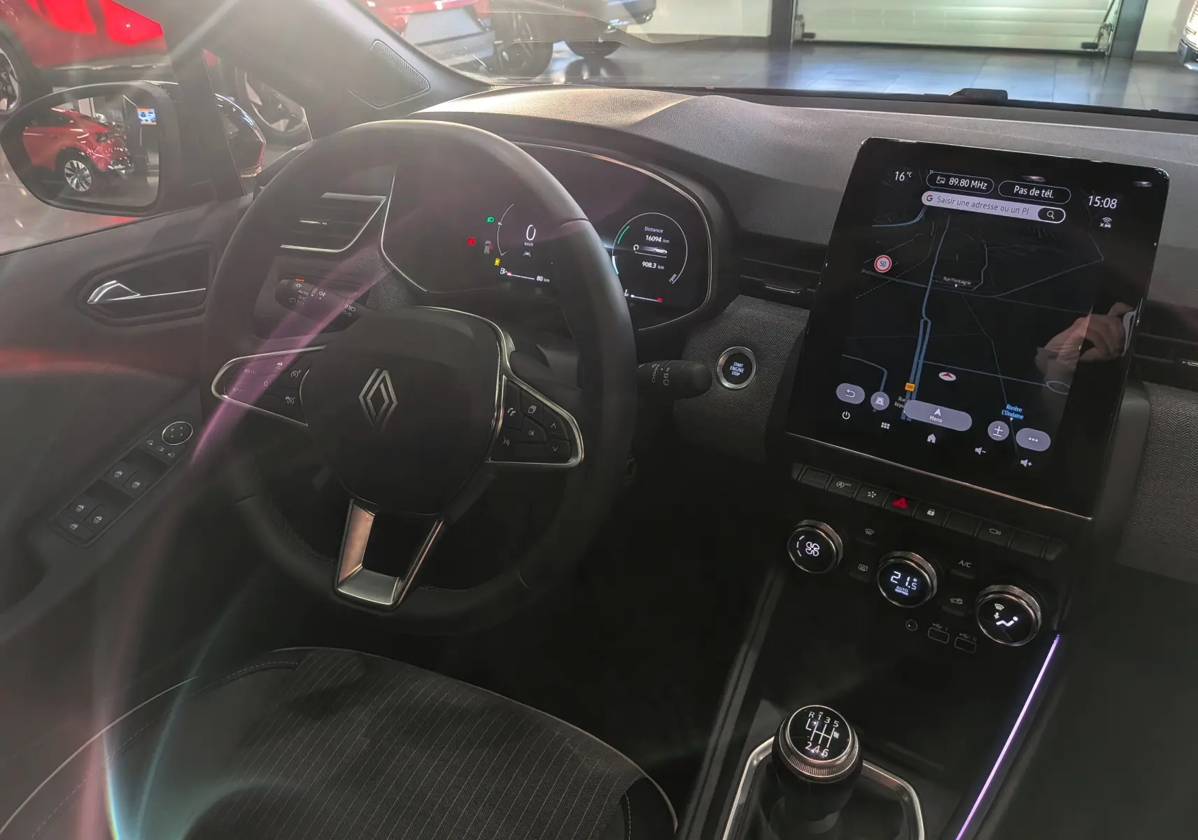 Vue intérieure côté conducteur de la Renault Clio V avec volant, tableau de bord numérique et écran central tactile allumé.