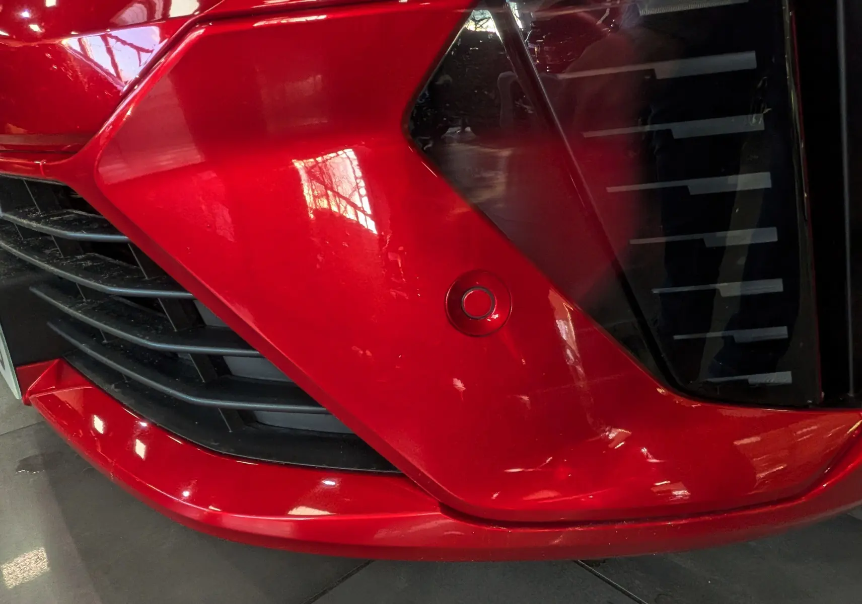 Gros plan sur le bouclier avant rouge flamme de la Renault Clio V ECO-100 CH TECHNO avec capteur de stationnement visible.