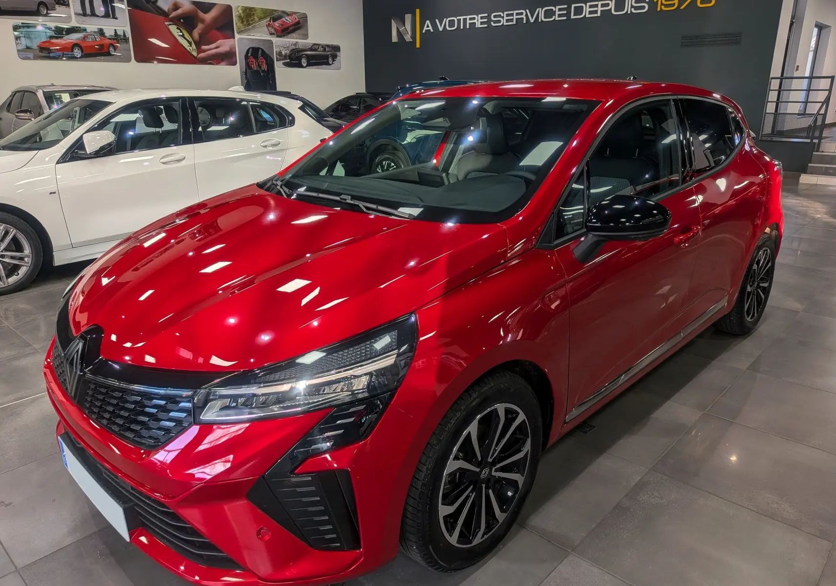 Renault Clio V Rouge Flamme vue 3/4 avant droit, avec jantes noires et détails noirs sur les rétroviseurs.