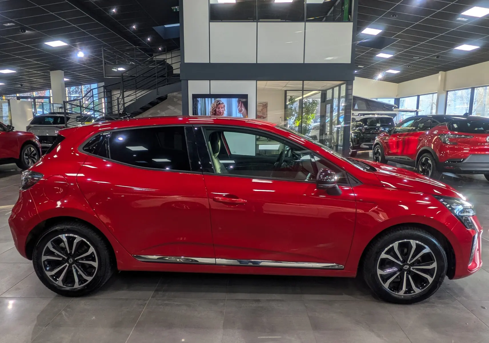 Profil côté gauche d'une Renault Clio V Rouge Flamme, avec jantes alliage et détails chromés visibles en concession.