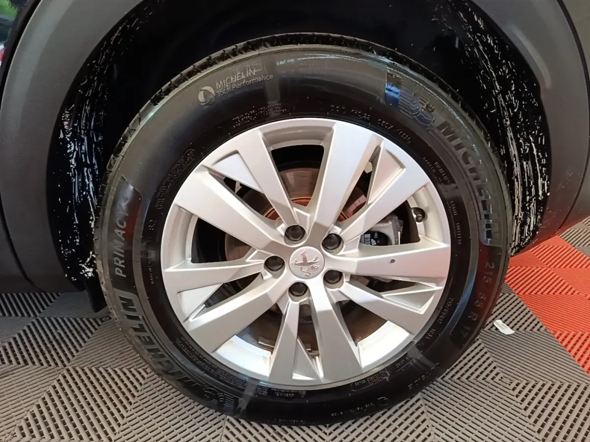 Gros plan sur la roue avant droite avec jante argentée et pneu Michelin du Peugeot 3008 noir 2022.
