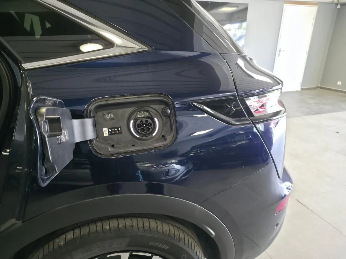 Vue arrière côté gauche du DS7 Crossback bleu avec trappe de recharge hybride ouverte et feux arrière distinctifs.