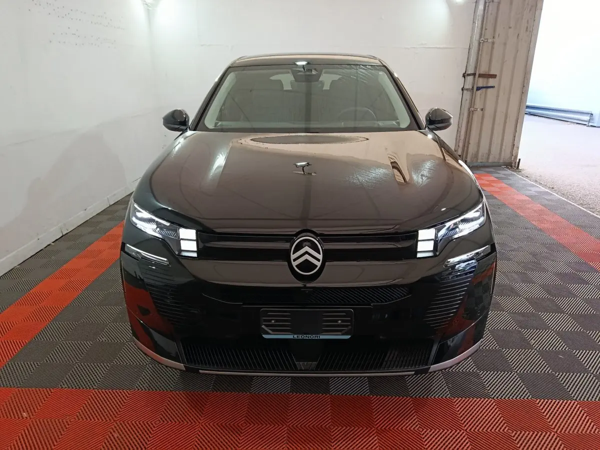 Vue avant d'une Citroën C5 hybride noire avec phares LED allumés dans un garage au sol carrelé rouge et gris.