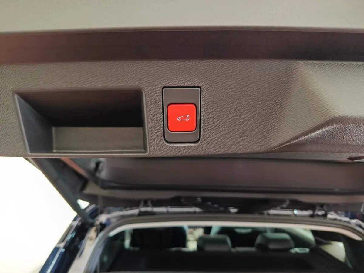 Bouton rouge d'ouverture électrique du coffre sur la partie intérieure du hayon d'une Citroën C5 noire, vue arrière ouverte.