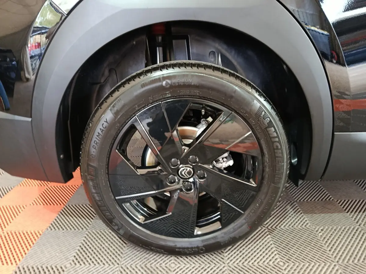 Gros plan sur la roue avant gauche noire avec jante en alliage noir brillant et logo Citroën au centre.