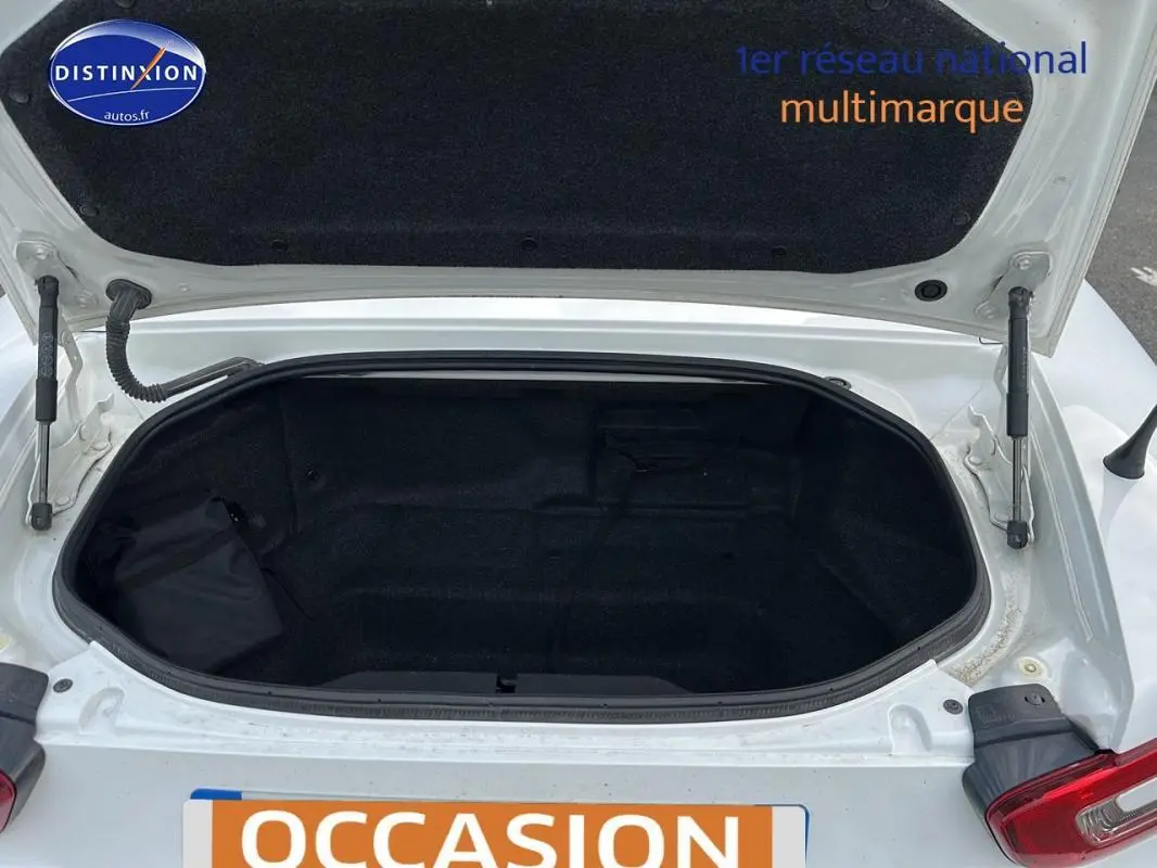 Coffre ouvert vu de dessus sur une FIAT 124 Spider blanc, montrant l'espace de rangement vide et la garniture noire intérieure.