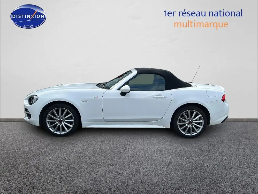 Profil côté gauche d'une FIAT 124 Spider blanche avec capote noire et jantes alliage 17 pouces.