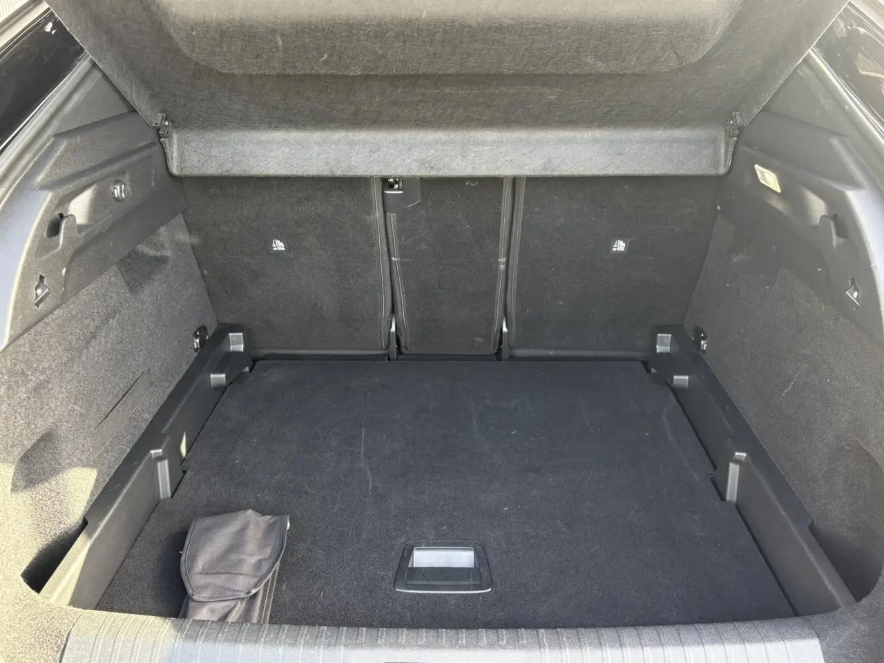 Coffre ouvert vu de l'arrière du Peugeot 3008 Hybrid 145 GT, intérieur noir avec tapis de sol et rangement intégré.