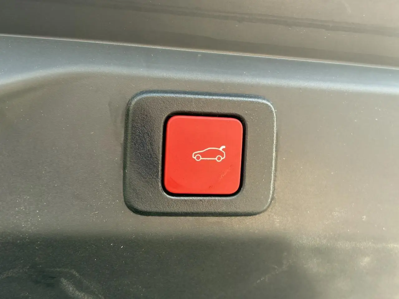 Bouton rouge de déverrouillage du hayon sur le coffre d'un Peugeot 3008 Hybrid 2025 gris Titane.