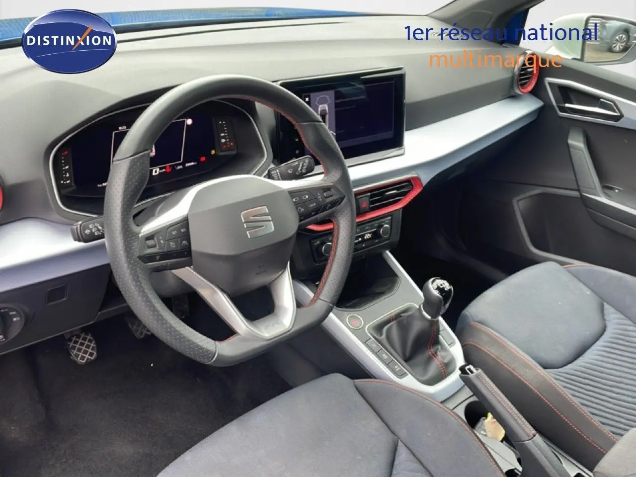Vue intérieure côté conducteur du SEAT Arona 2025, volant cuir multifonction et levier de vitesse manuelle, ambiance noire avec touches rouges.