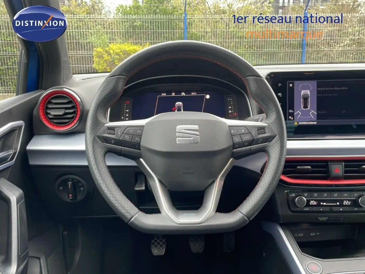 Vue centrée du volant perforé et tableau de bord numérique d’un SEAT Arona bleu saphir 2025 avec détails rouges intérieurs.