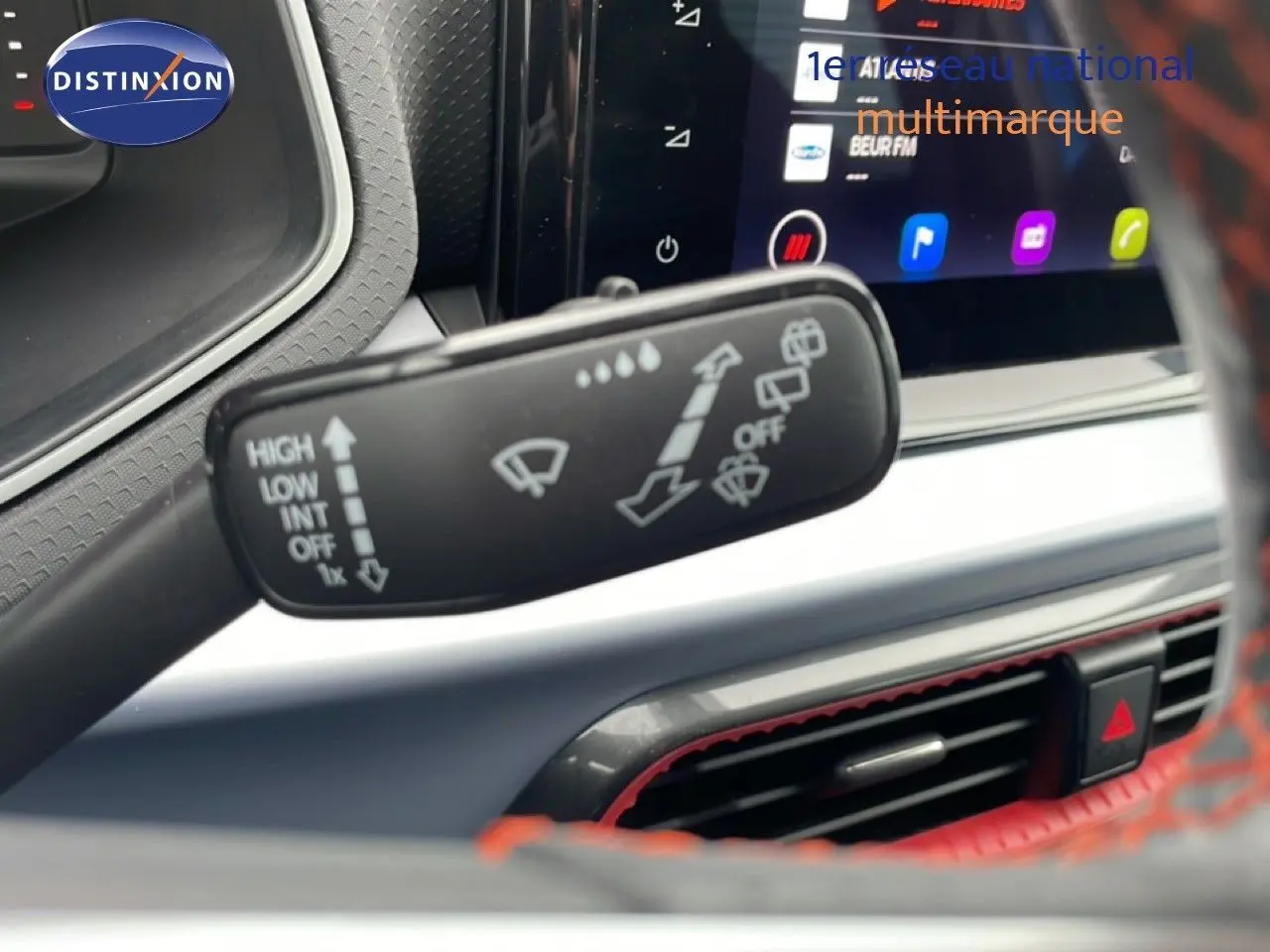 Gros plan sur la commande d’essuie-glace dans l’habitacle du SEAT Arona bleu saphir avec écran tactile et volant rouge.