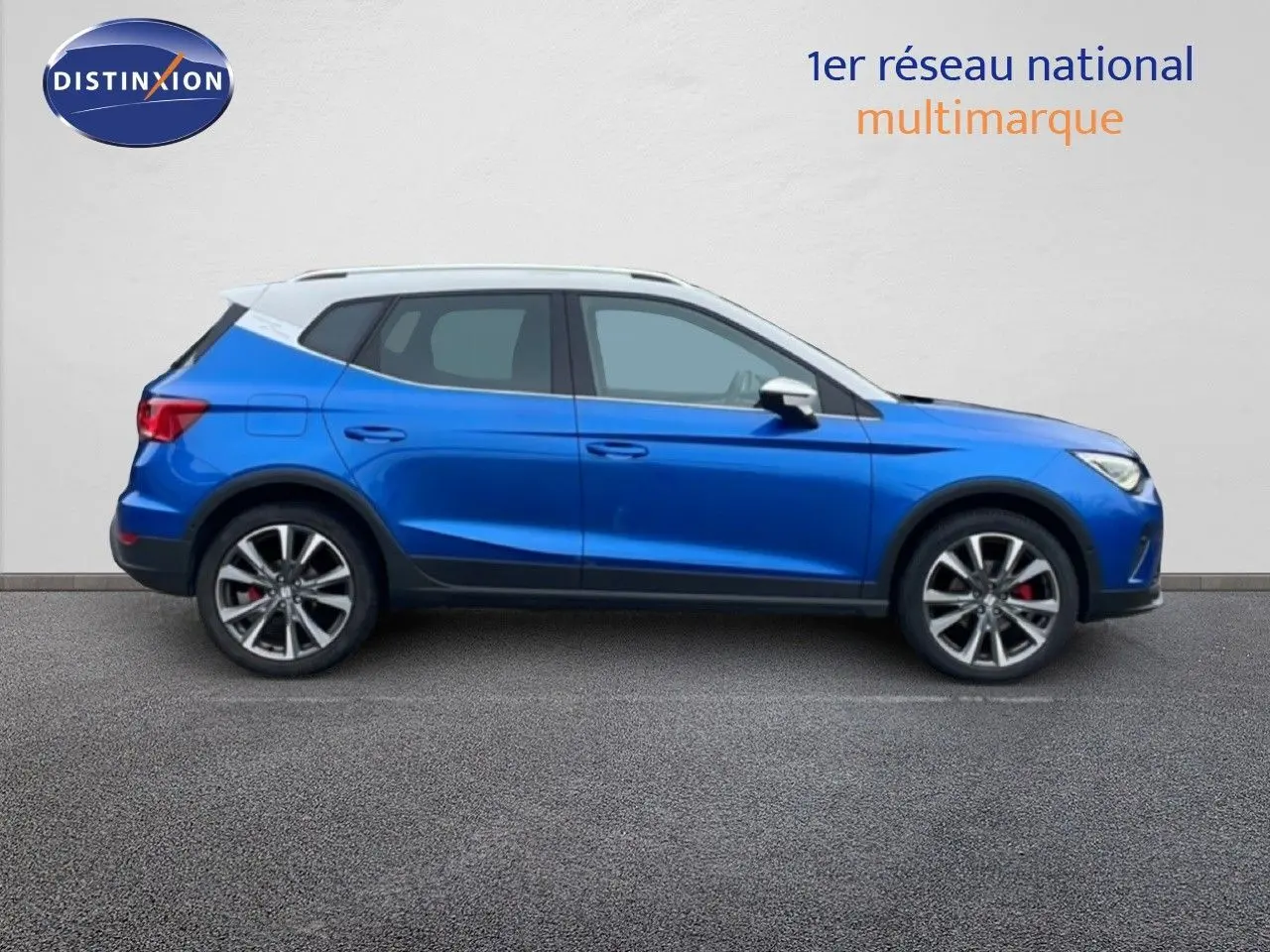 Vue de profil côté gauche d'un SEAT Arona bleu saphir avec toit blanc, jantes alliage et étriers rouges visibles.