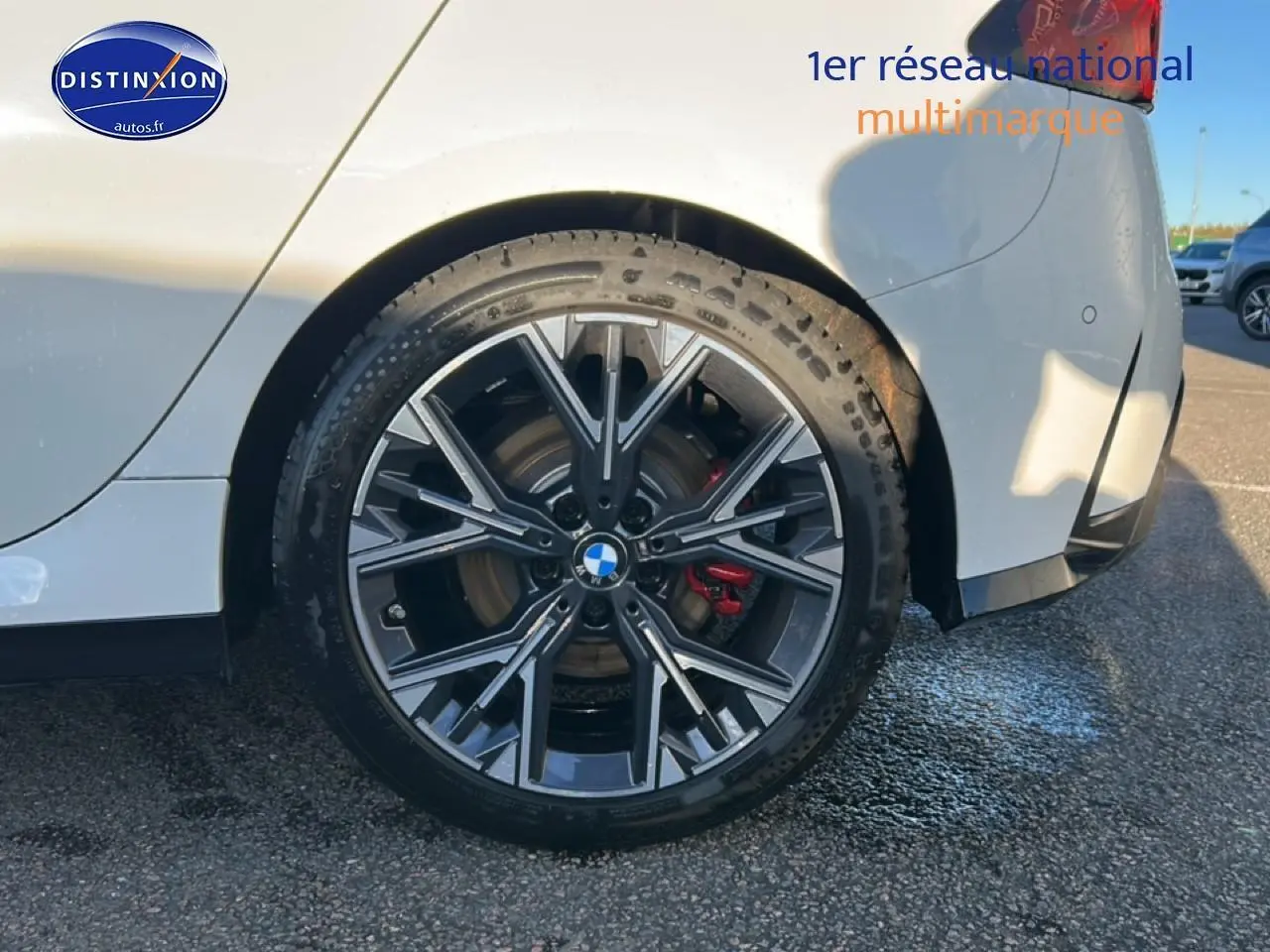 Gros plan sur la roue arrière droite d'une BMW Série 1 blanche avec jante 18 pouces bicolore et étrier de frein rouge.