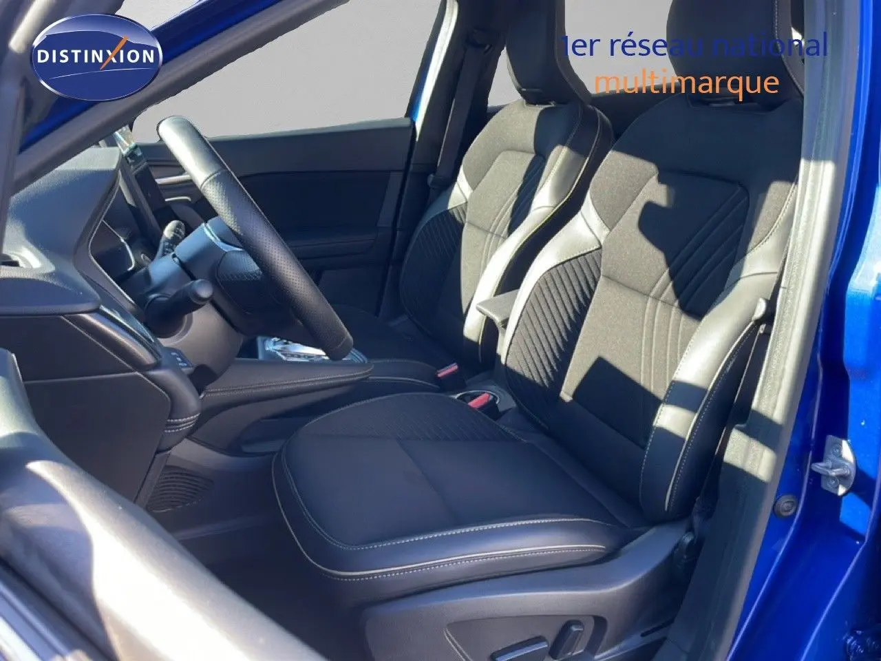 Vue intérieure côté conducteur de la Renault Symbioz 2025 bleu iron metal, sièges tissu noir avec surpiqûres blanches.