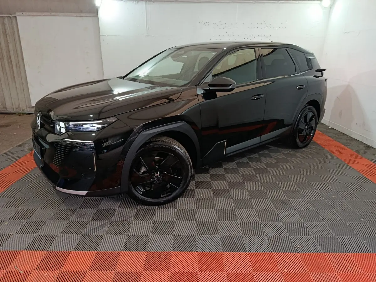 Vue 3/4 avant droit du SUV Citroën C5 hybride noir, avec jantes noires et phares LED allumés dans un garage.