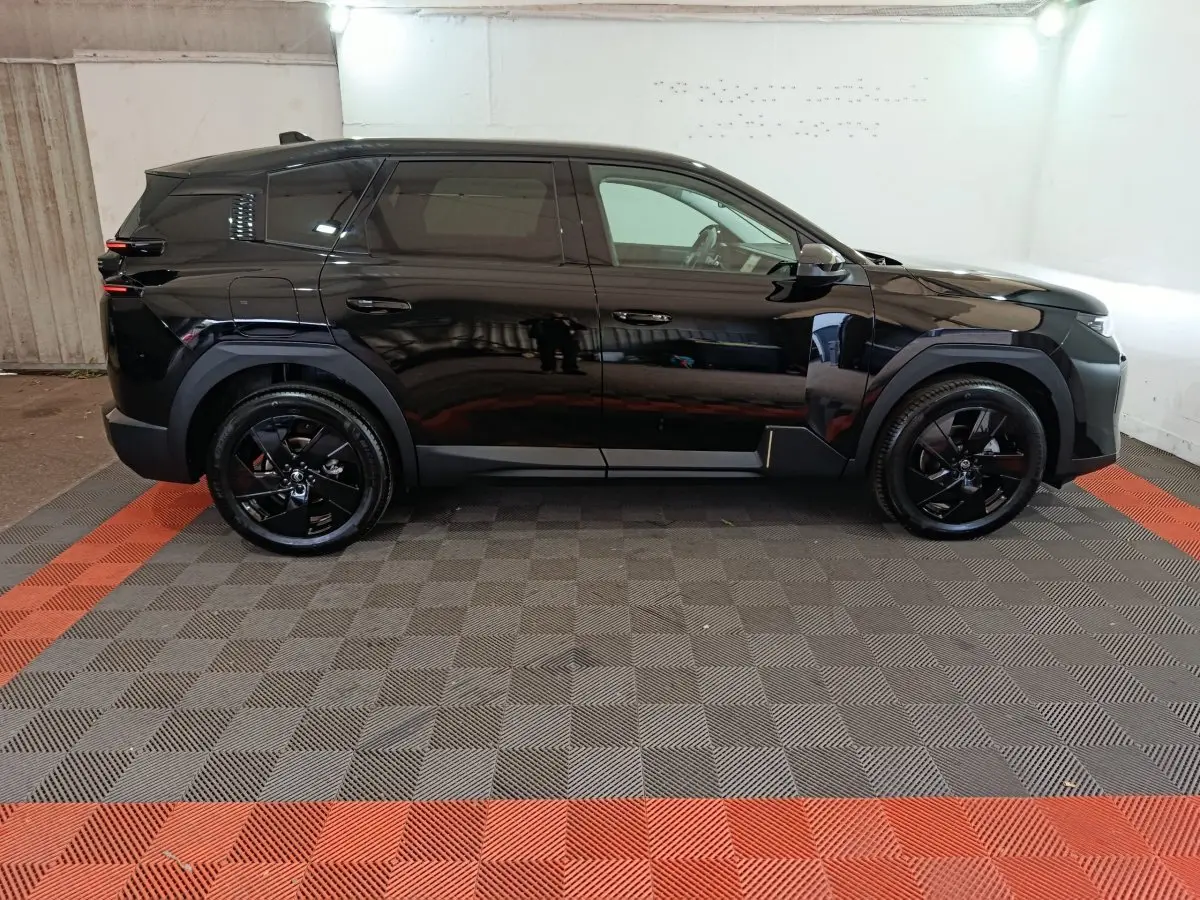 Vue de profil côté gauche d'une Citroën C5 Hybride noire avec jantes noires dans un garage éclairé.