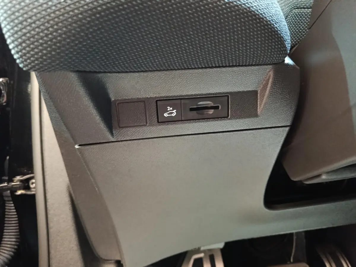 Détail intérieur montrant le bouton d'ouverture du coffre sur la partie inférieure du tableau de bord noir du Citroën C5 Hybride.