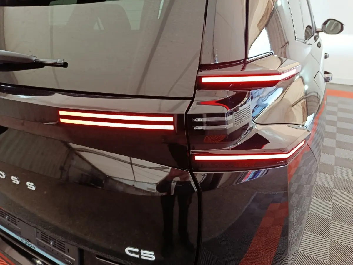 Feu arrière droit allumé d'une Citroën C5 noire, vue rapprochée du coin arrière avec reflets sur la carrosserie.