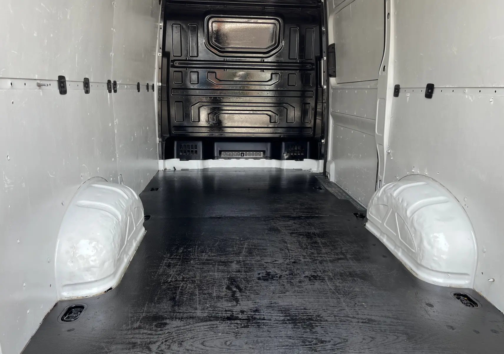 Intérieur du fourgon Volkswagen Crafter blanc vu de l'arrière, montrant l'espace de chargement vide avec parois blanches et plancher noir.