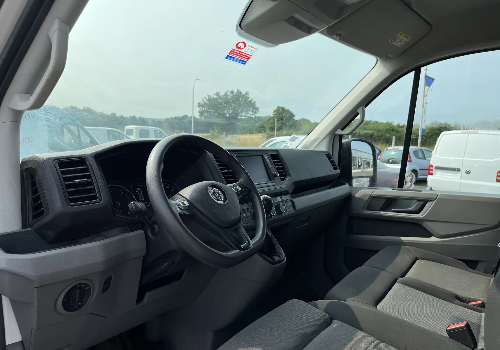 Intérieur côté conducteur du Volkswagen Crafter blanc 2019, tableau de bord et sièges en tissu gris visibles de profil droit.