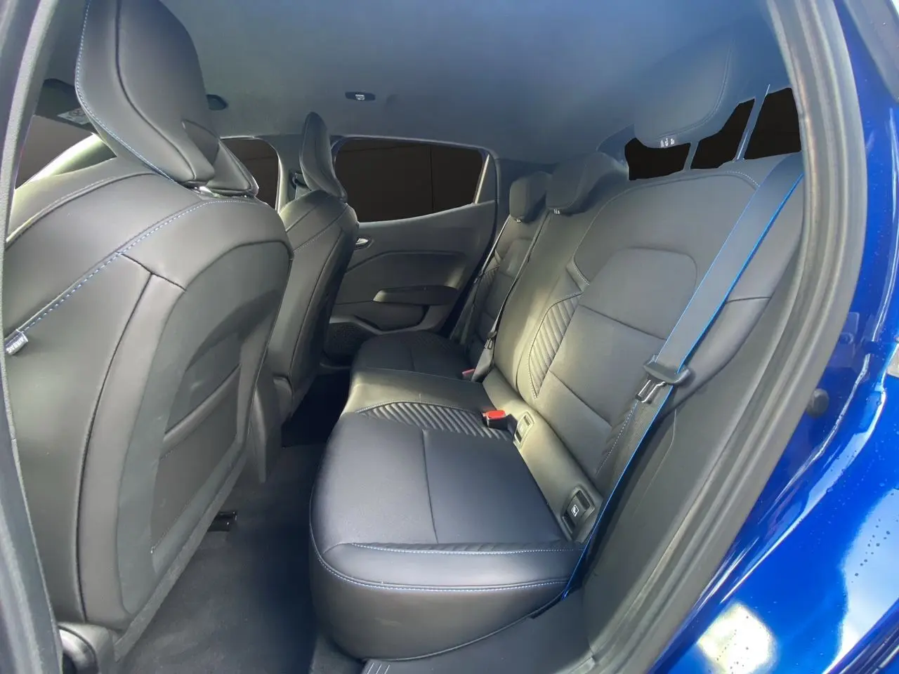 Vue intérieure arrière droite de la Renault Clio V TCE 90 Esprit Alpine avec sellerie noire et surpiqûres bleues, portière ouverte.