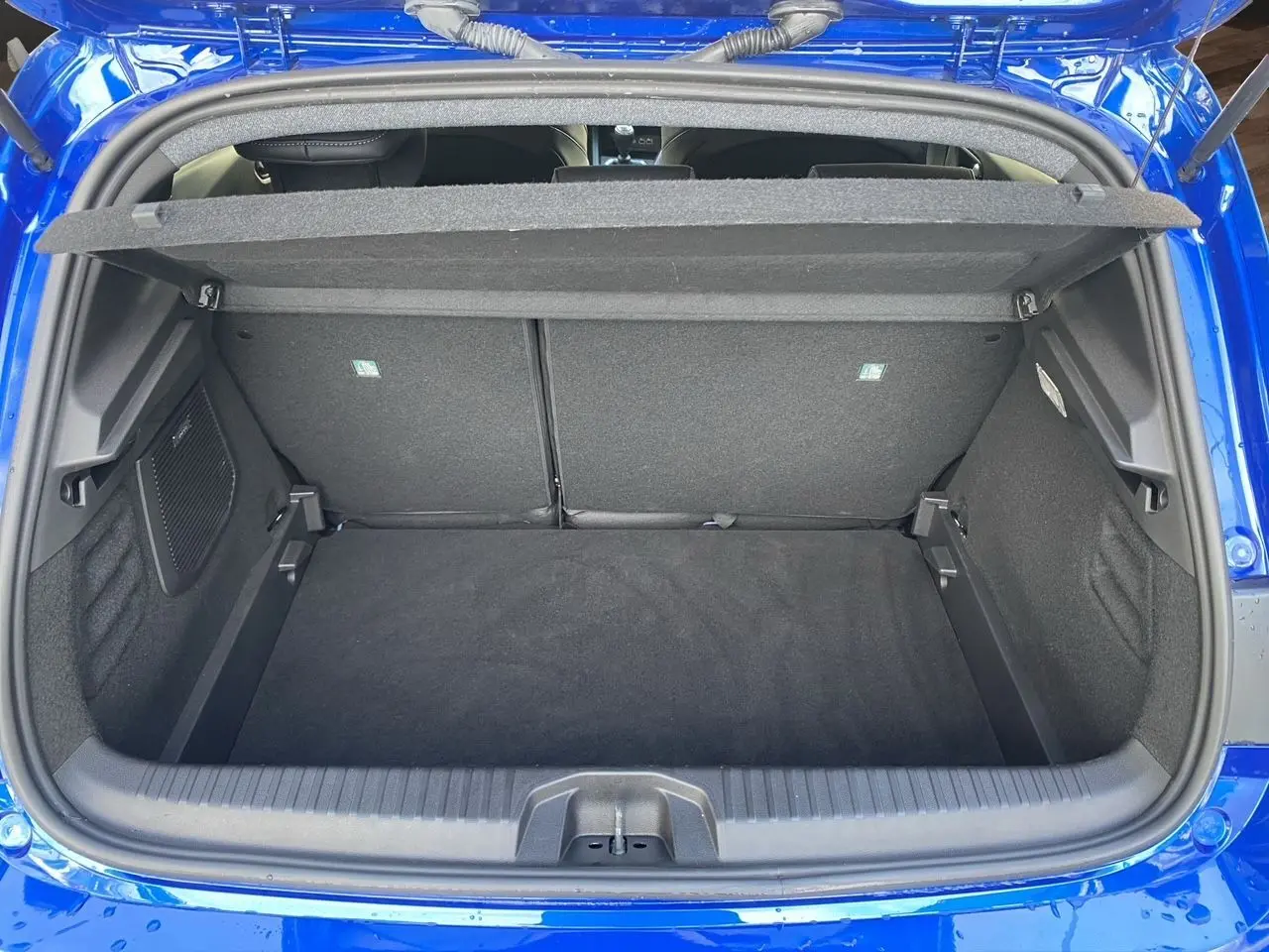 Coffre ouvert vu de l'arrière d'une Renault Clio V TCE 90 Esprit Alpine en bleu Iron, intérieur noir et tapis de coffre.