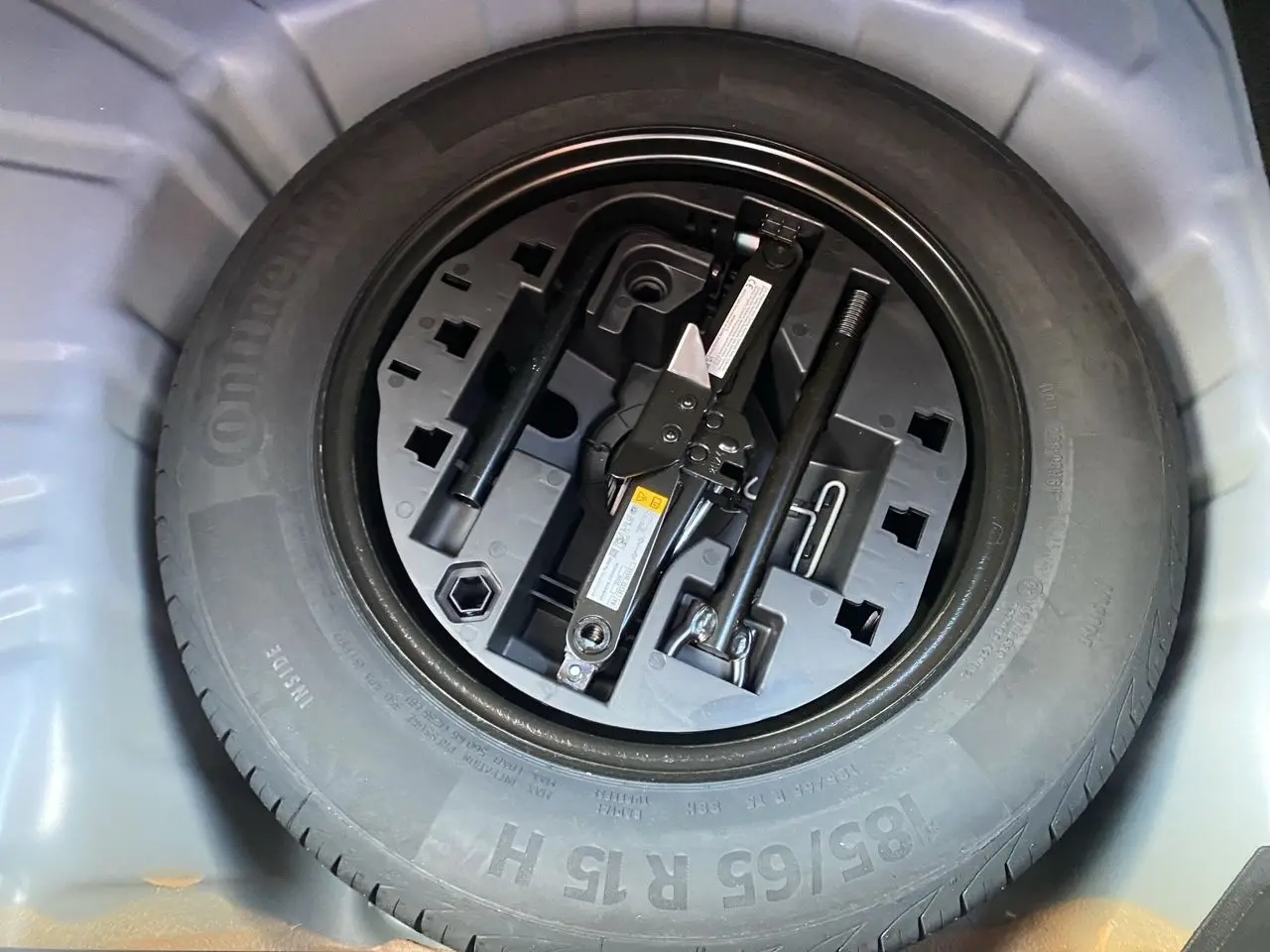 Vue en plongée sur la roue de secours et le cric dans le coffre d'une Renault Clio V bleu Iron 2025.