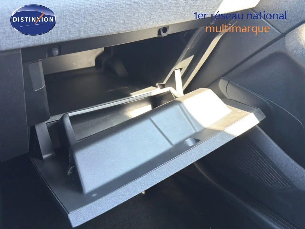 Gros plan sur la boîte à gants ouverte côté passager d'une Renault Clio blanche, intérieur noir visible.