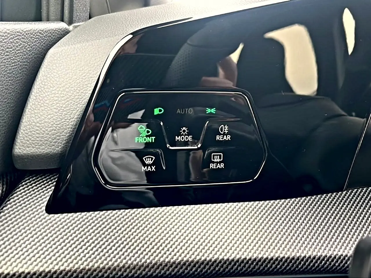 Gros plan sur les commandes d’éclairage et de désembuage avec finition noire brillante et insert carbone dans une Volkswagen Golf noire 2026.