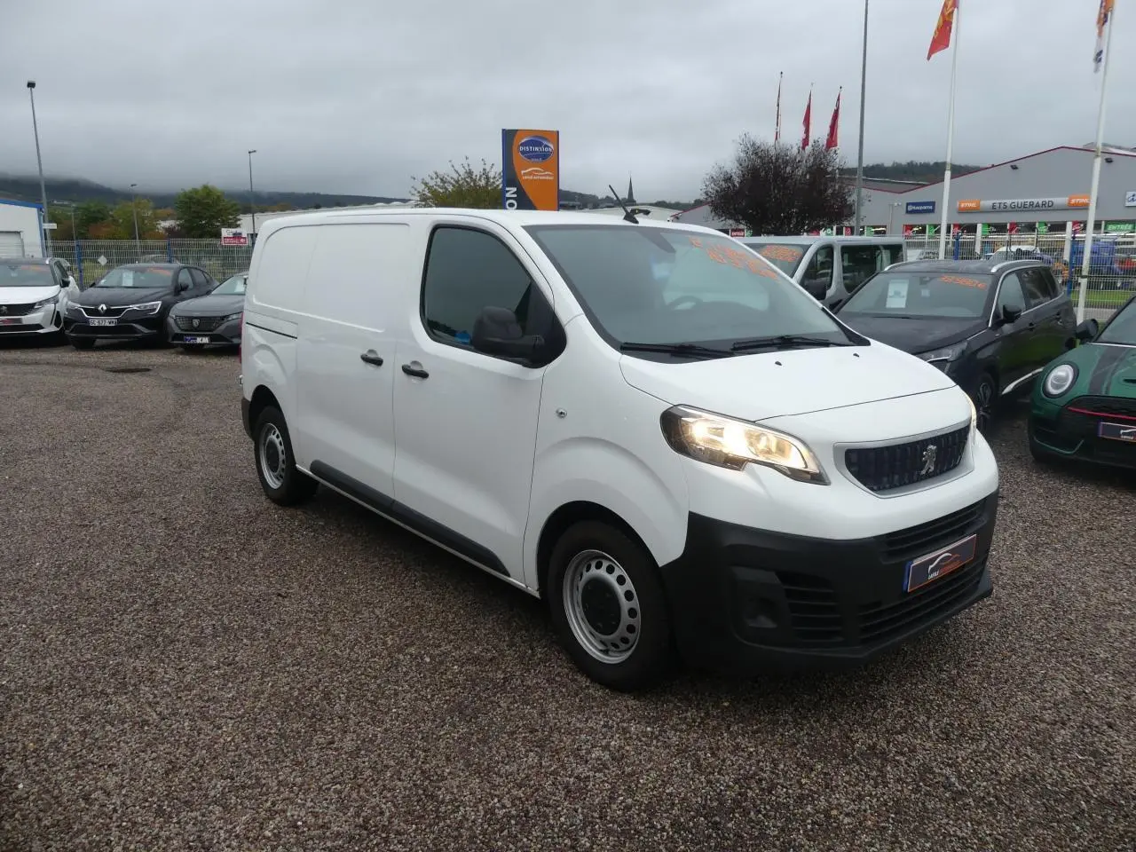 Fourgon Peugeot Expert blanc vu en 3/4 avant droit avec phares allumés sur parking extérieur.