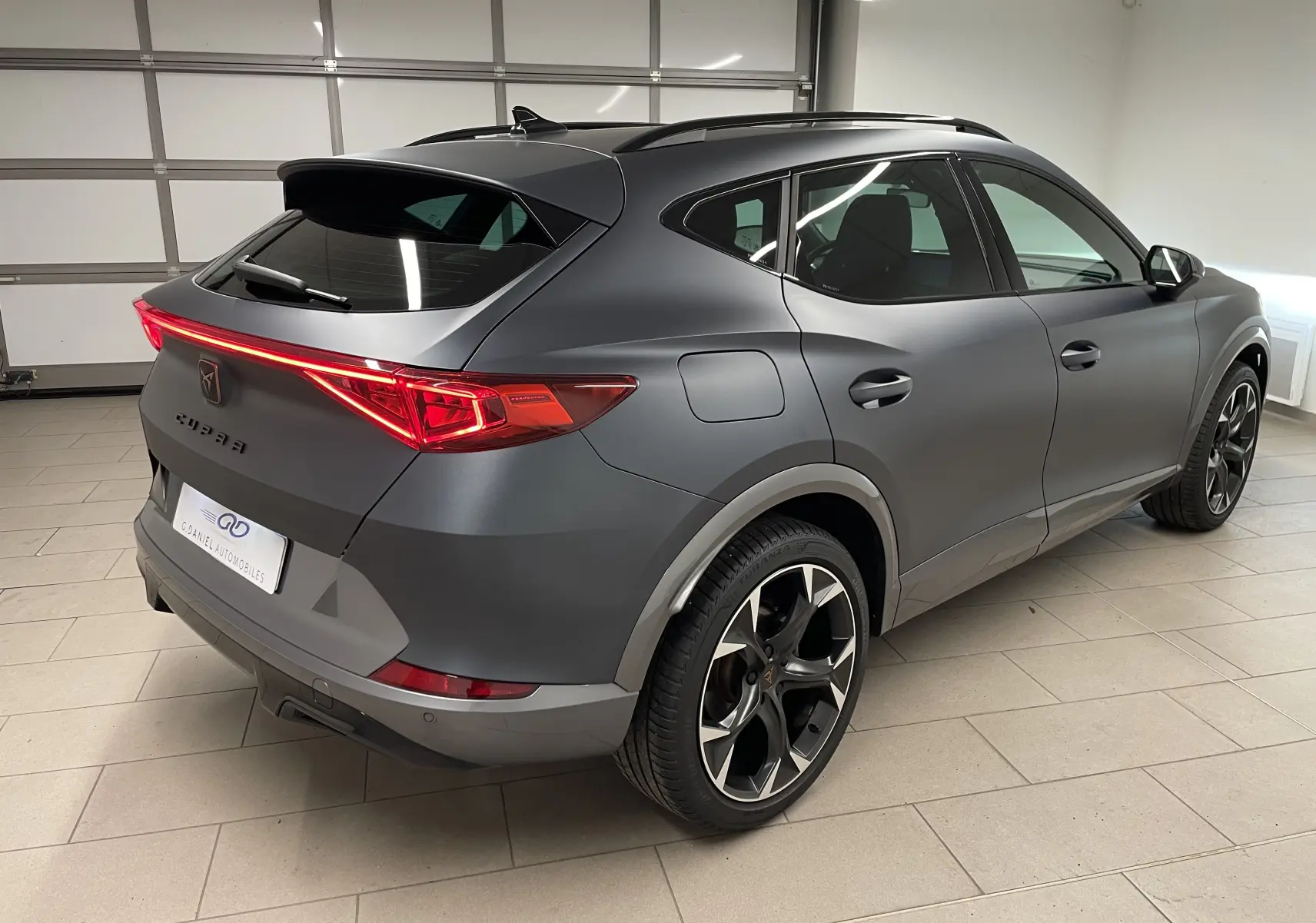 Vue 3/4 arrière droit du CUPRA Formentor 1.5 TSI 150 DSG7 VZ-LINE en gris magnétique mat avec feux arrière allumés.
